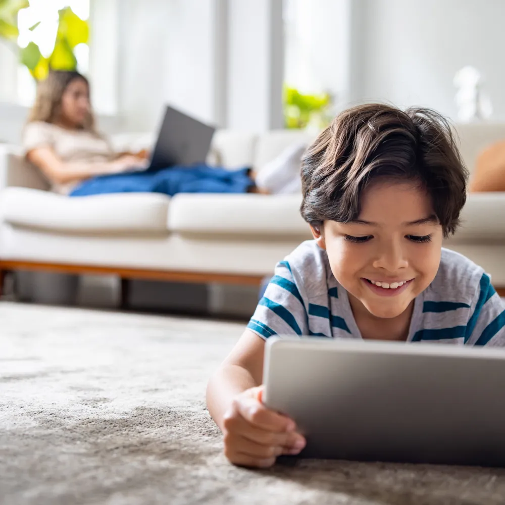 Young boy watching a  tablet with parent in the background.
